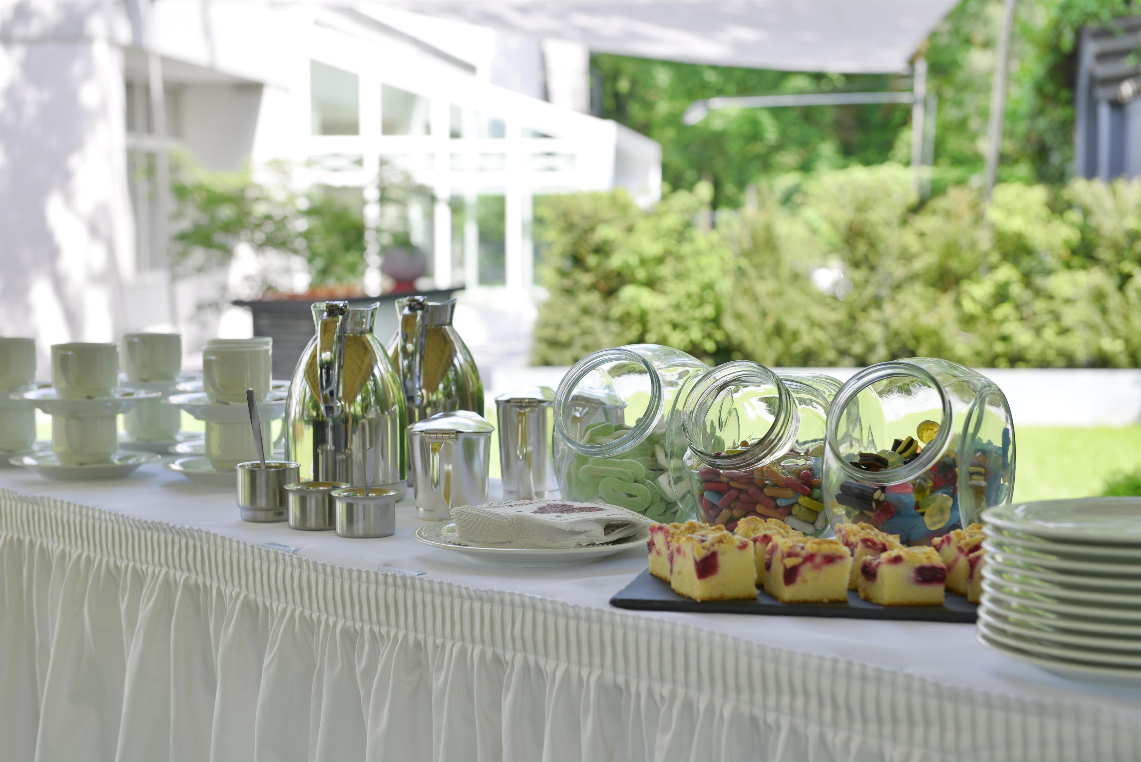 Ein reichhaltiges Buffet mit verschiedenen Speisen, darunter Süßigkeiten und Gebäck, sowie eine Auswahl an Tassen und kleinen Schalen.