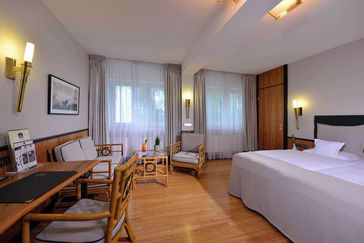 Une chambre d’hôtel avec un lit, un bureau avec des chaises, une petite table avec une plante et un tableau au mur.