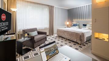 A hotel room with a bed, a desk with a laptop, a chair, and a TV.