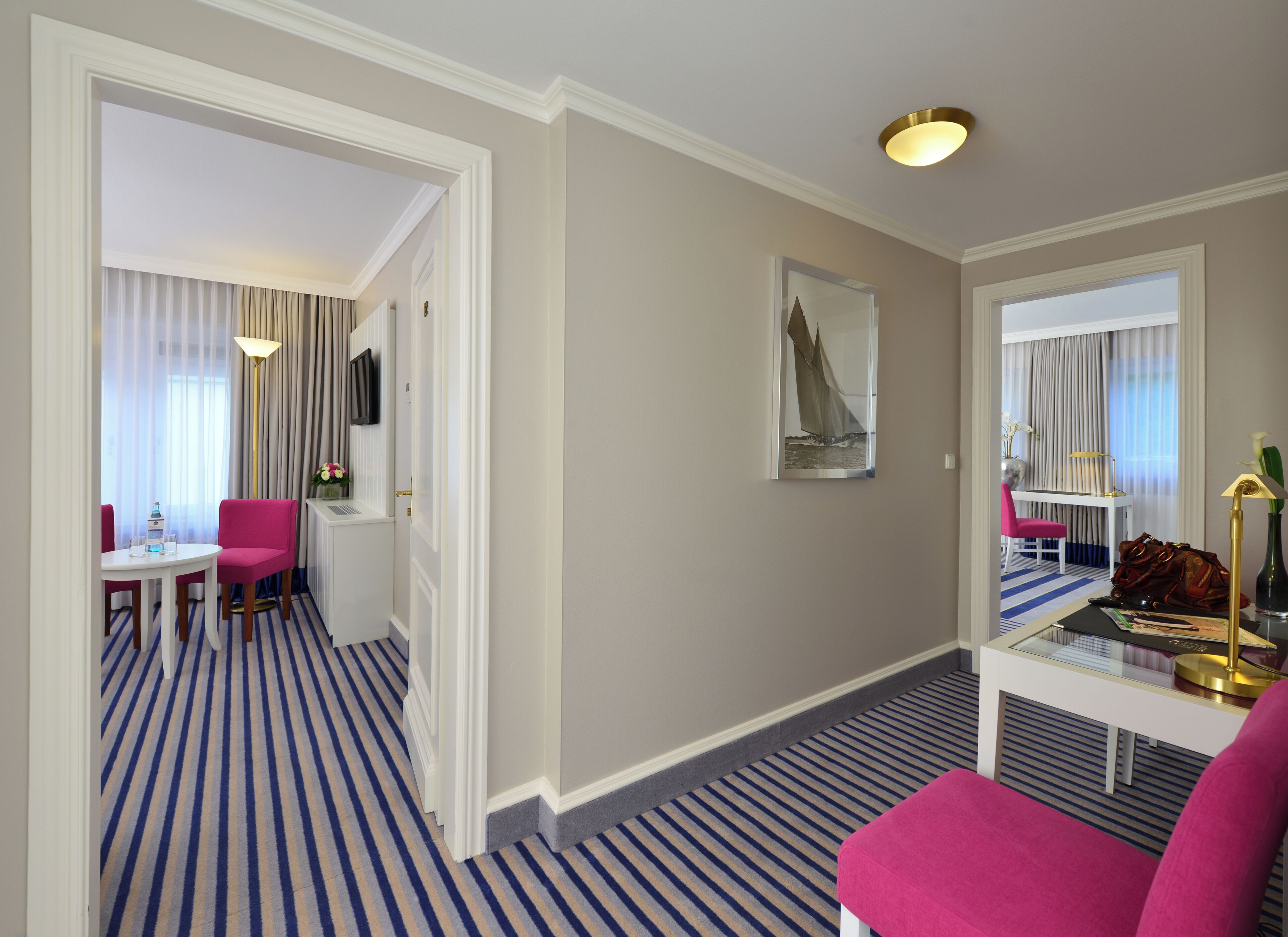A hotel room with a striped carpet, a desk with a chair, a bed, and a large mirror.