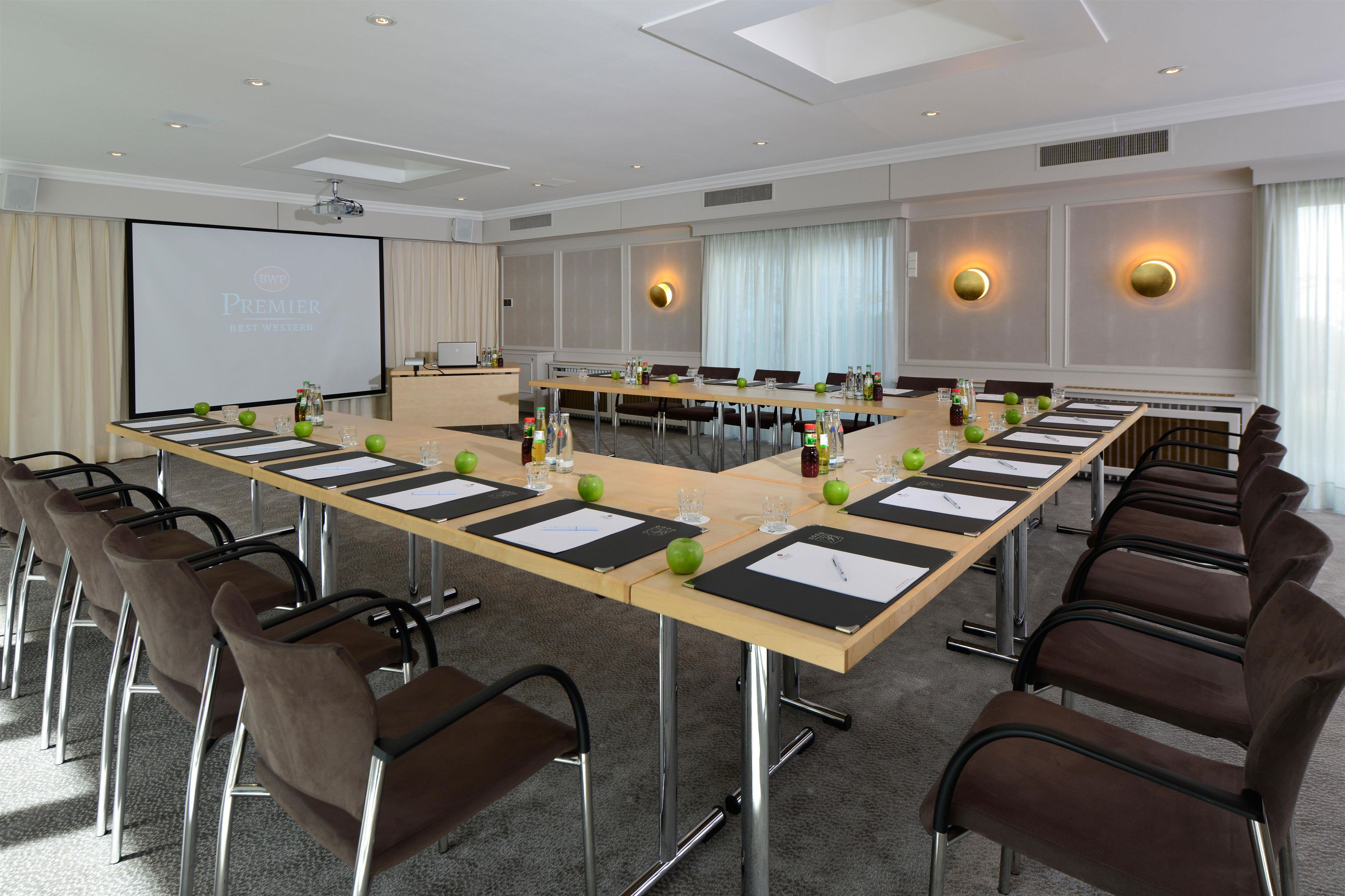 A conference room with a long table, chairs, a projector screen, and a presentation screen.