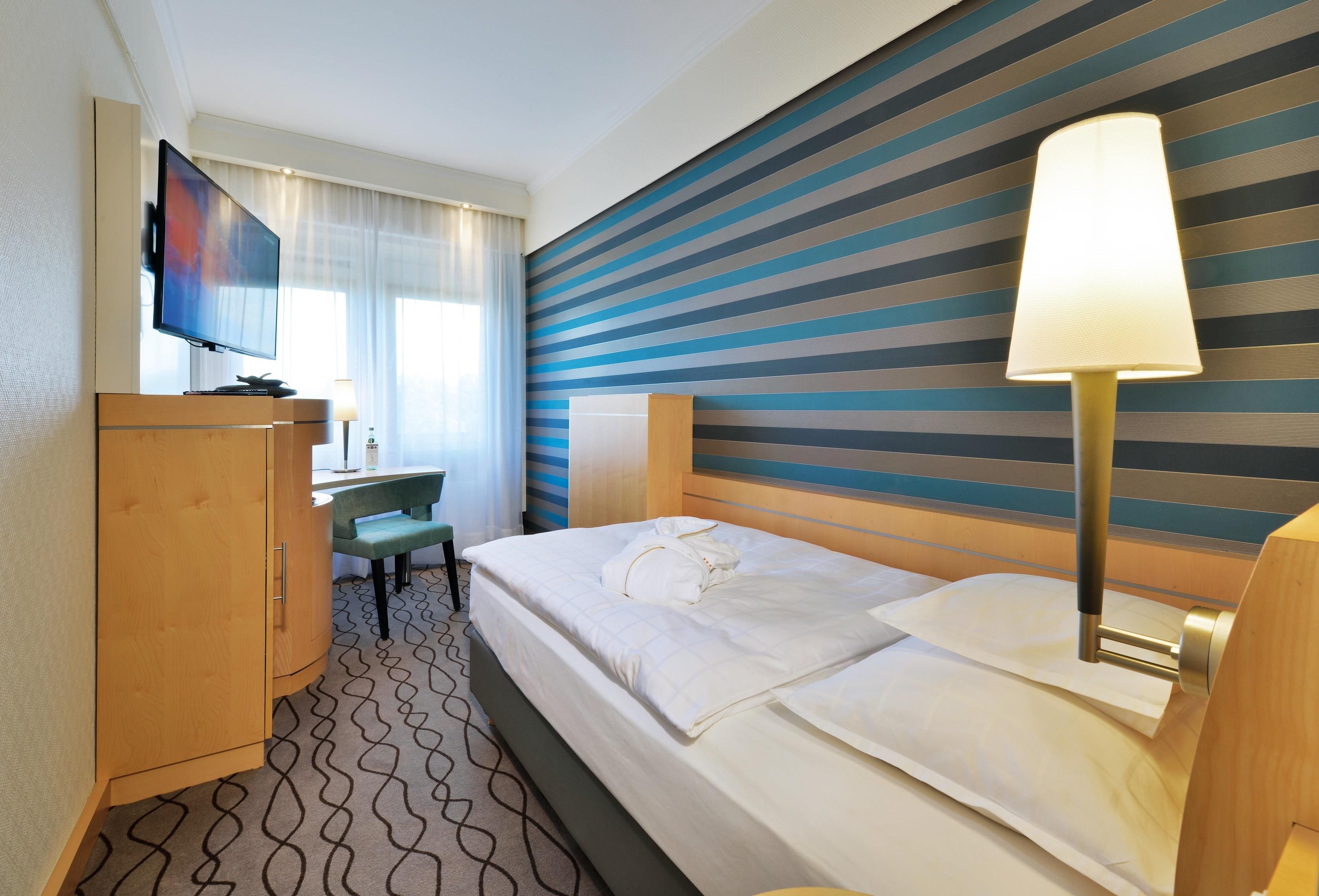 A hotel room with a bed, a desk, a television, and a striped wall.