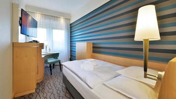 A hotel room with a bed, a desk, a television, and a striped wall.