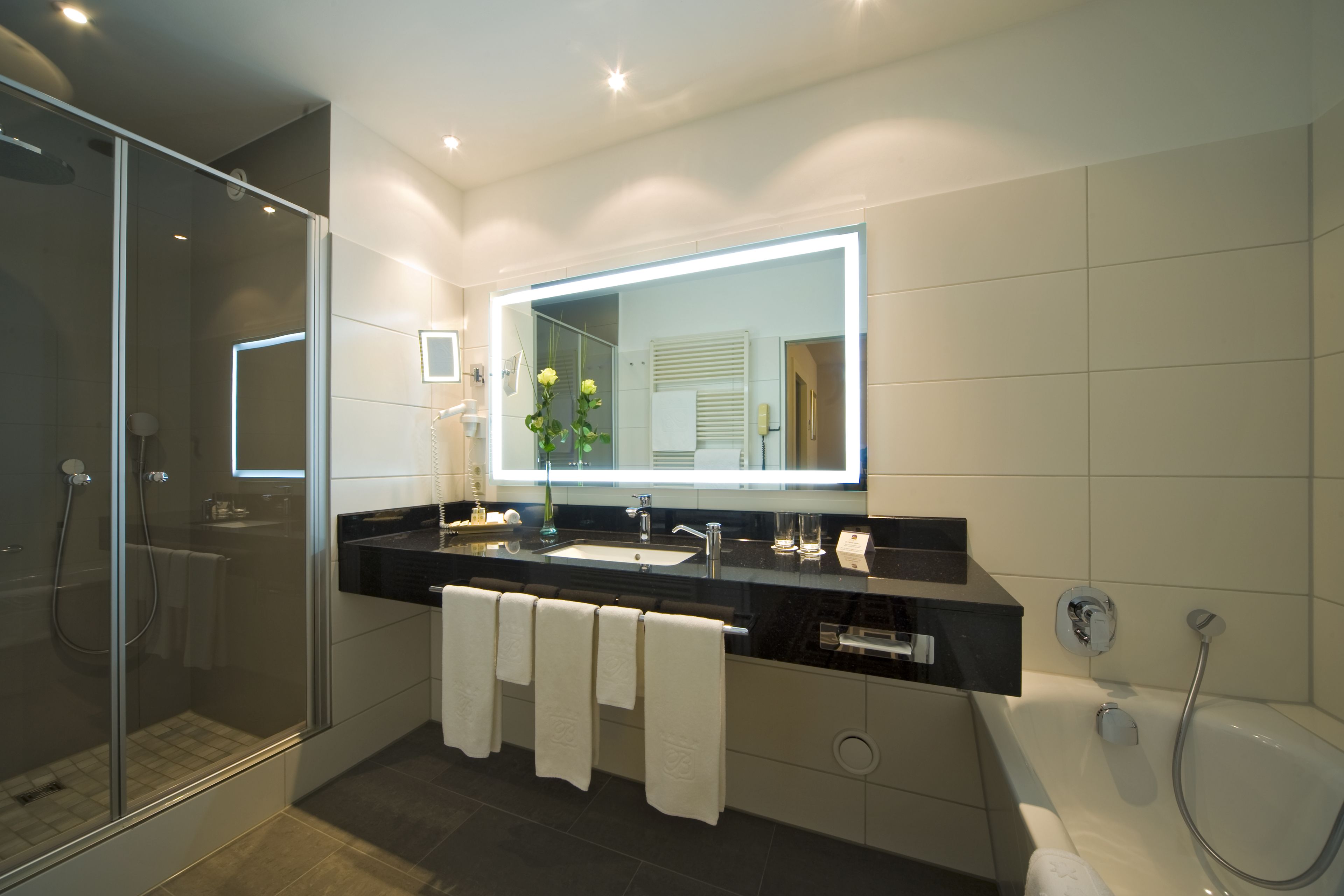 A modern bathroom with a glass-enclosed shower, a large mirror, and a bathtub.