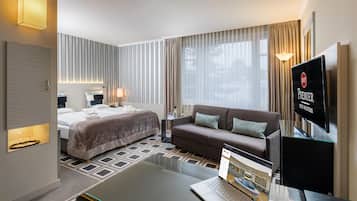 Ein Hotelzimmer mit einem Bett, einem Sofa, einem Fernseher, einem Laptop und einem Glastisch.