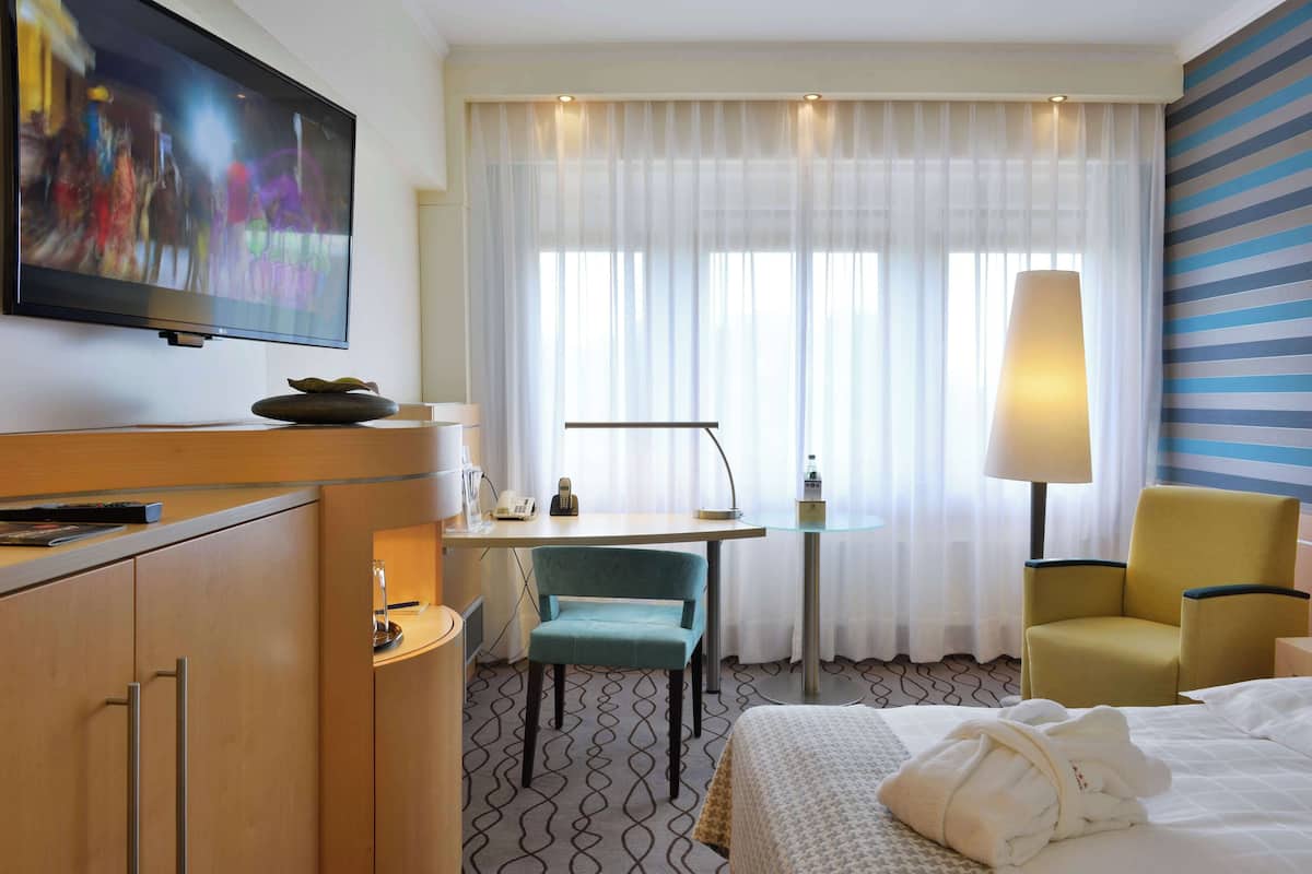 Une chambre d’hôtel comprenant un lit, un bureau avec une chaise, une télévision et une lampe.