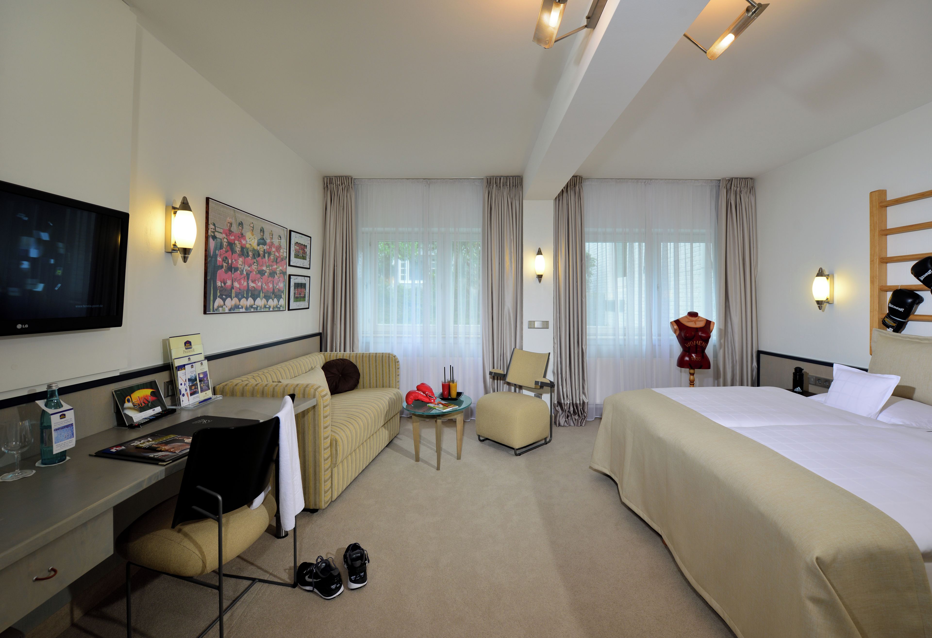Habitación de hotel con cama, escritorio, silla, televisor y ventana con cortinas.