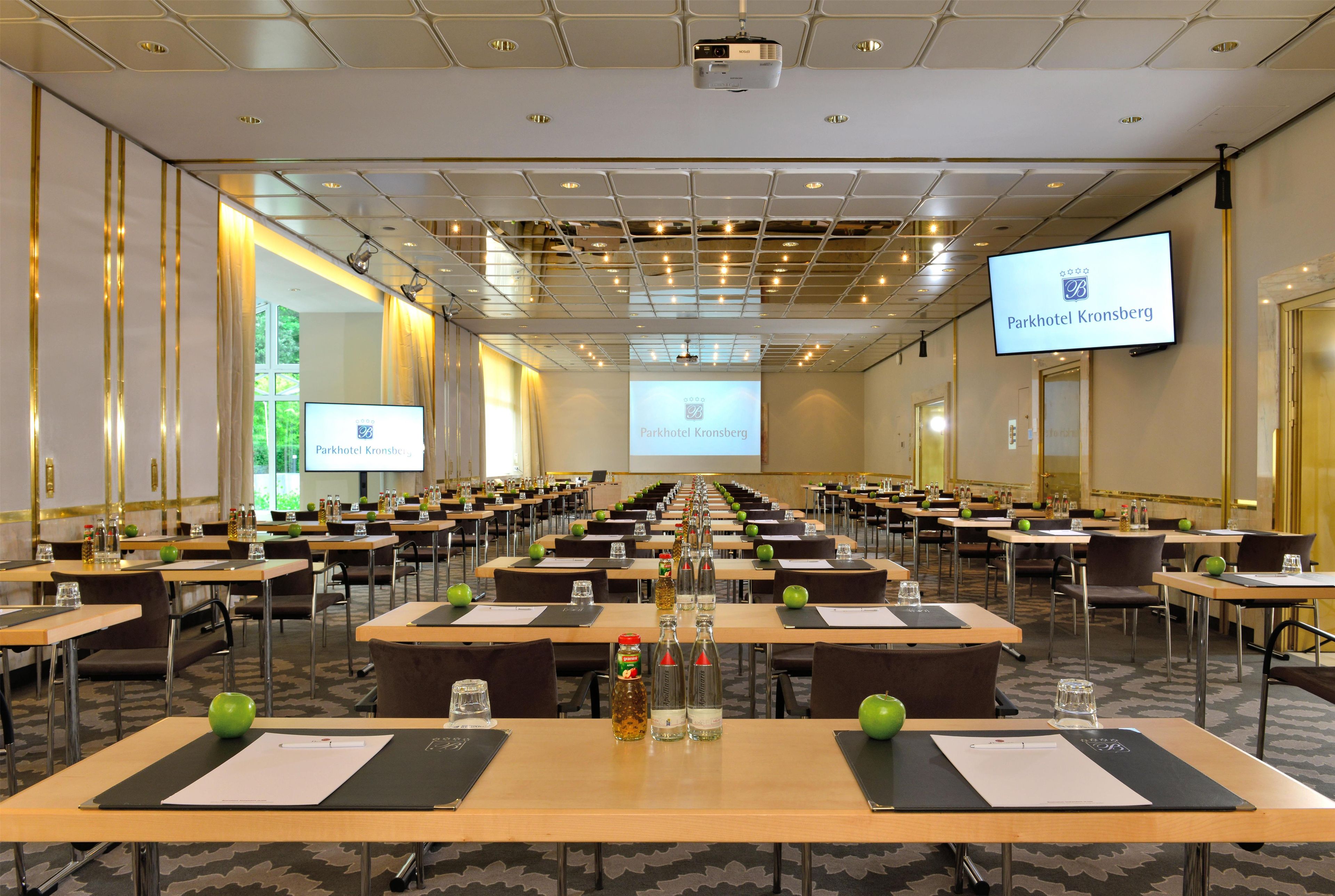 A conference room with rows of tables, chairs, and a large screen displaying the Parkhotel Kronberg logo.