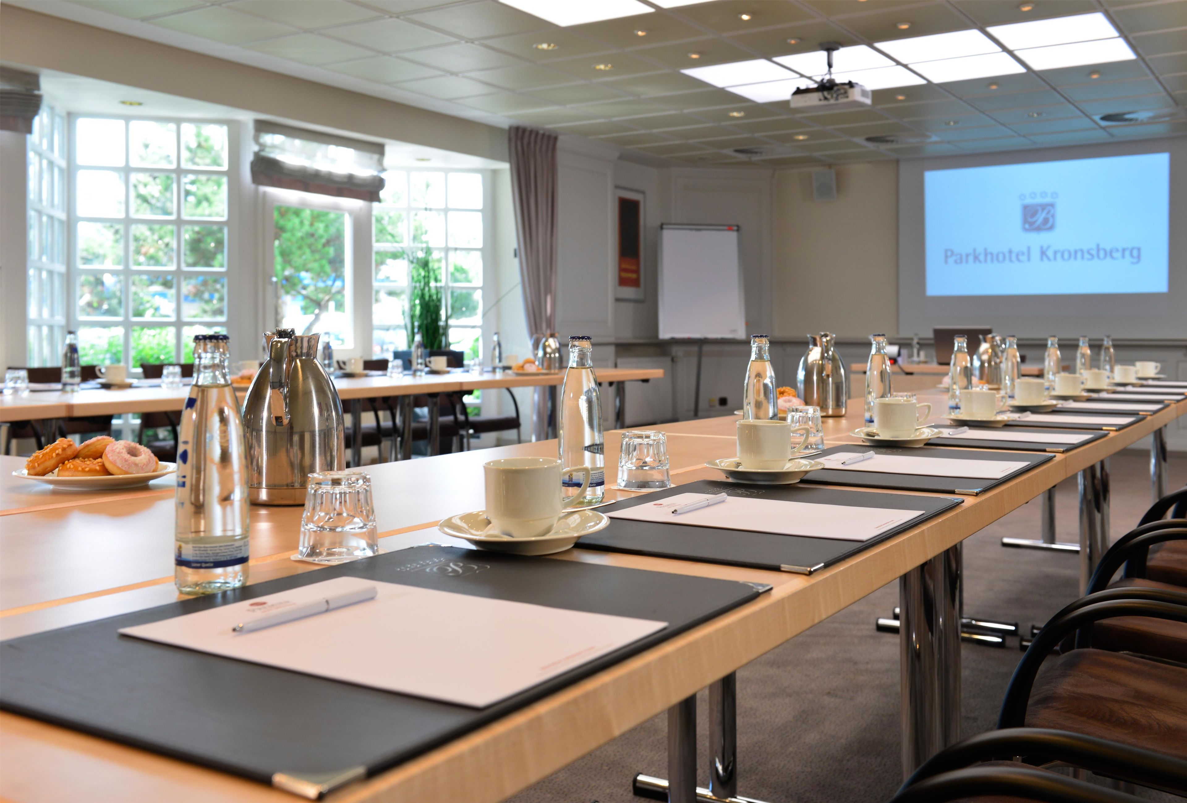 Ett konferensrum med ett långt bord uppdukat för ett möte, utrustat med vattenflaskor, glas och anteckningsblock.