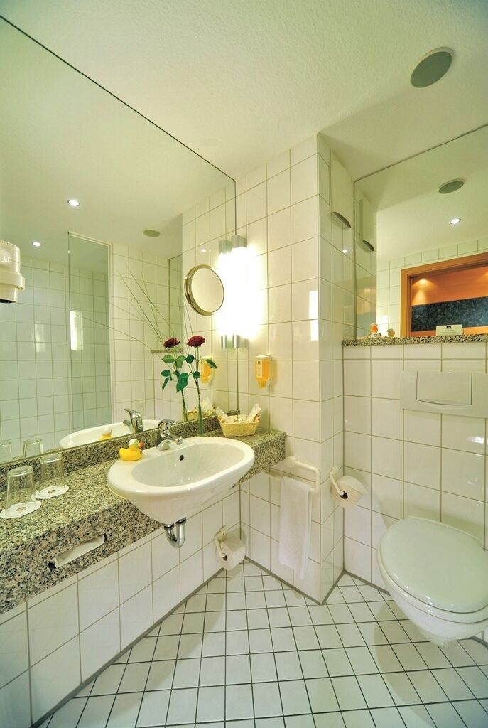 Un bagno con lavandino bianco, specchio e servizi igienici. È presente un porta asciugamani e un piccolo ripiano con articoli da toilette.