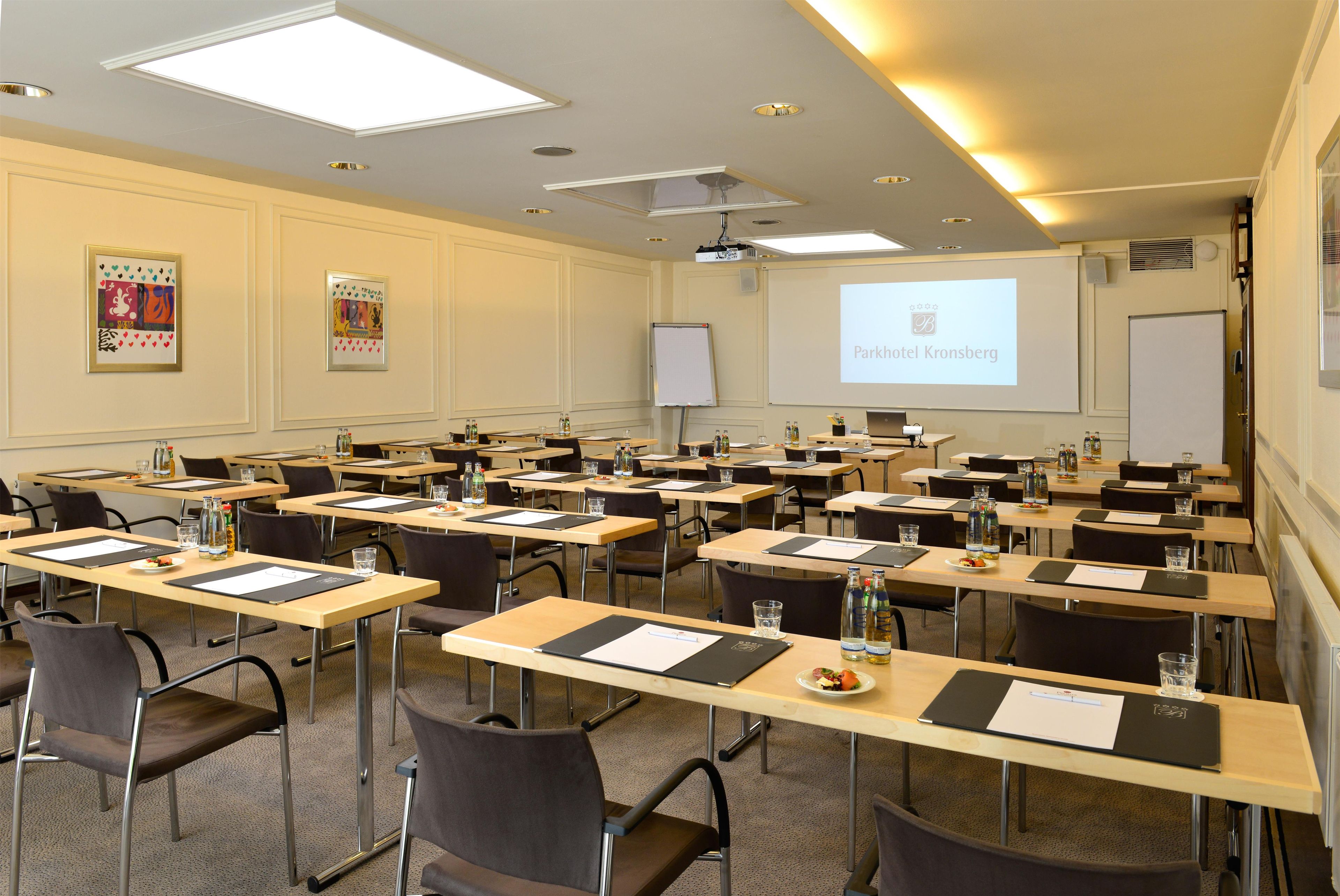 Un salón de conferencias con varias mesas, sillas y una pantalla para presentaciones.