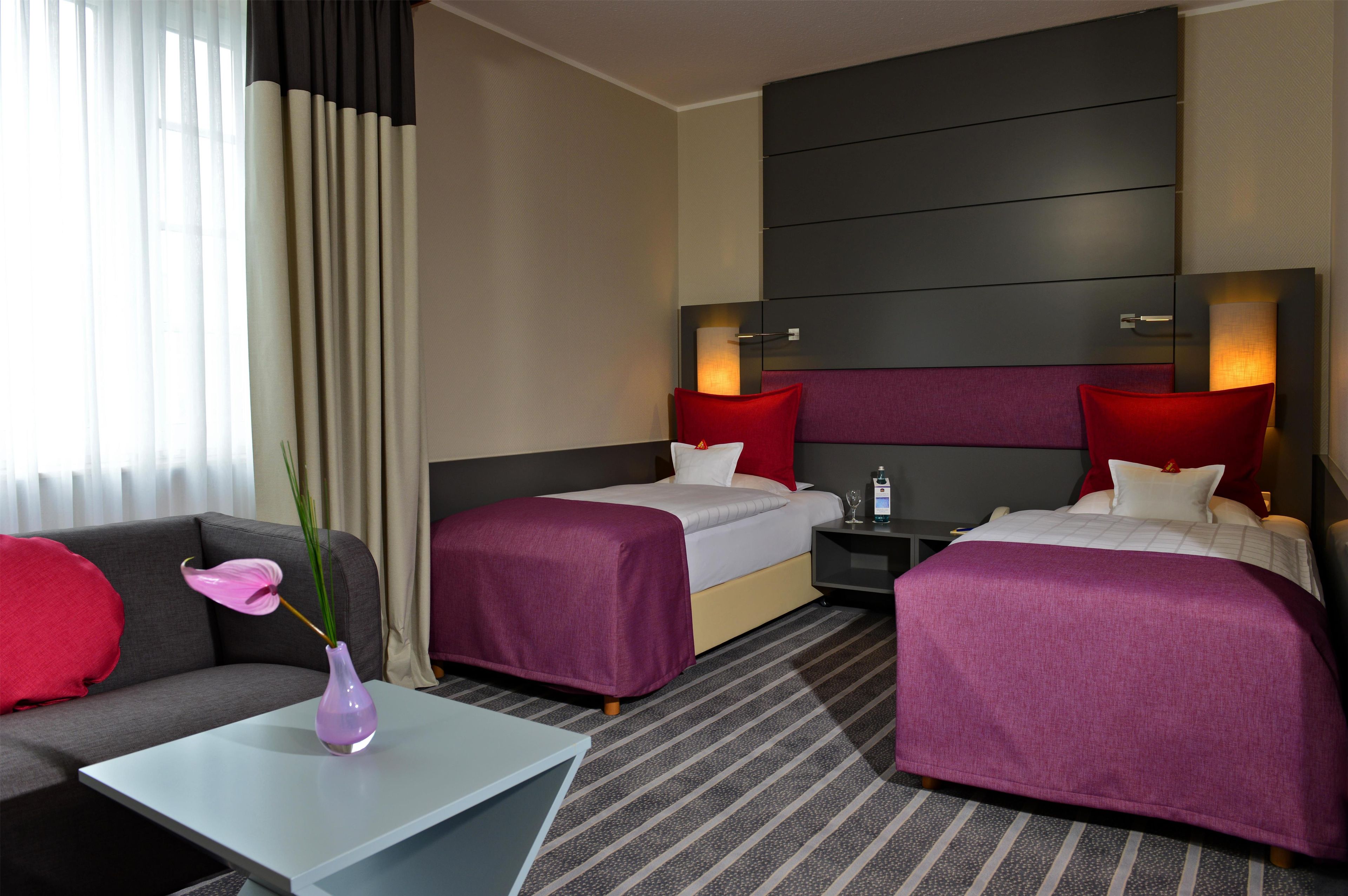 A hotel room with two beds, a sofa, a small table, and a vase with a plant.