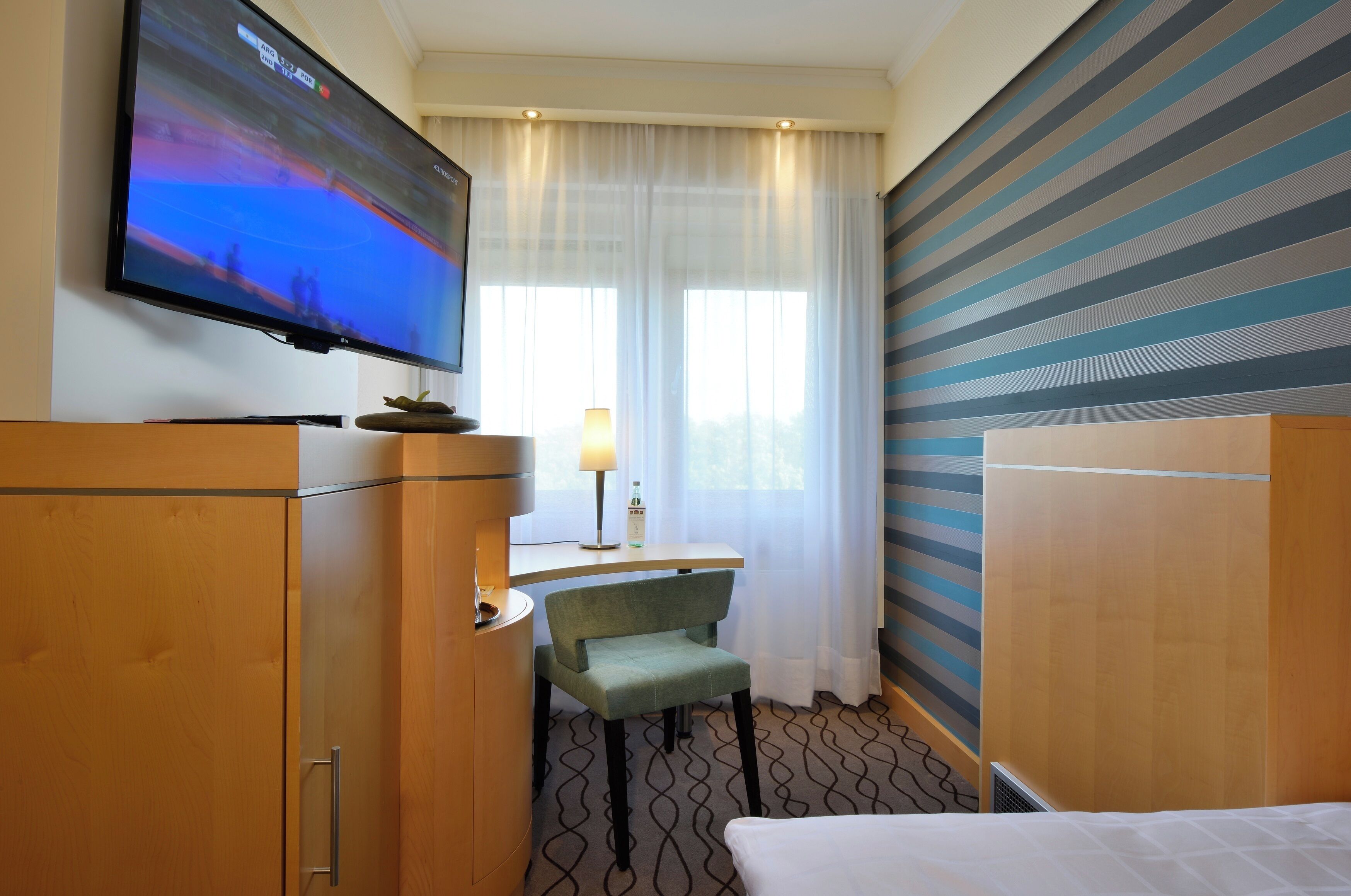Une chambre d’hôtel équipée d’une télévision, d’un bureau avec une lampe, d’une chaise et d’un lit.