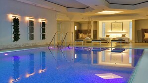 A modern hotel room with a large, reflective pool, a seating area with a sofa and chairs, and a staircase leading to another level.