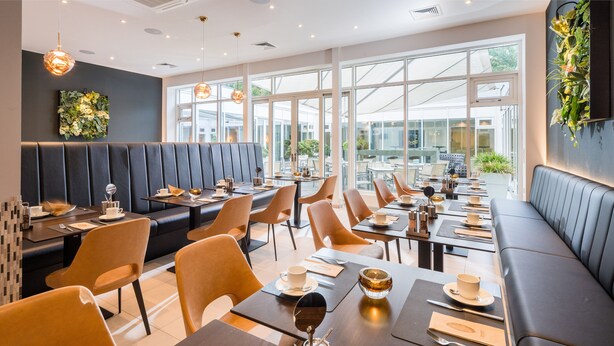 Een modern restaurant met hoge tafels en zitjes, grote ramen en uitzicht op het omliggende landschap.