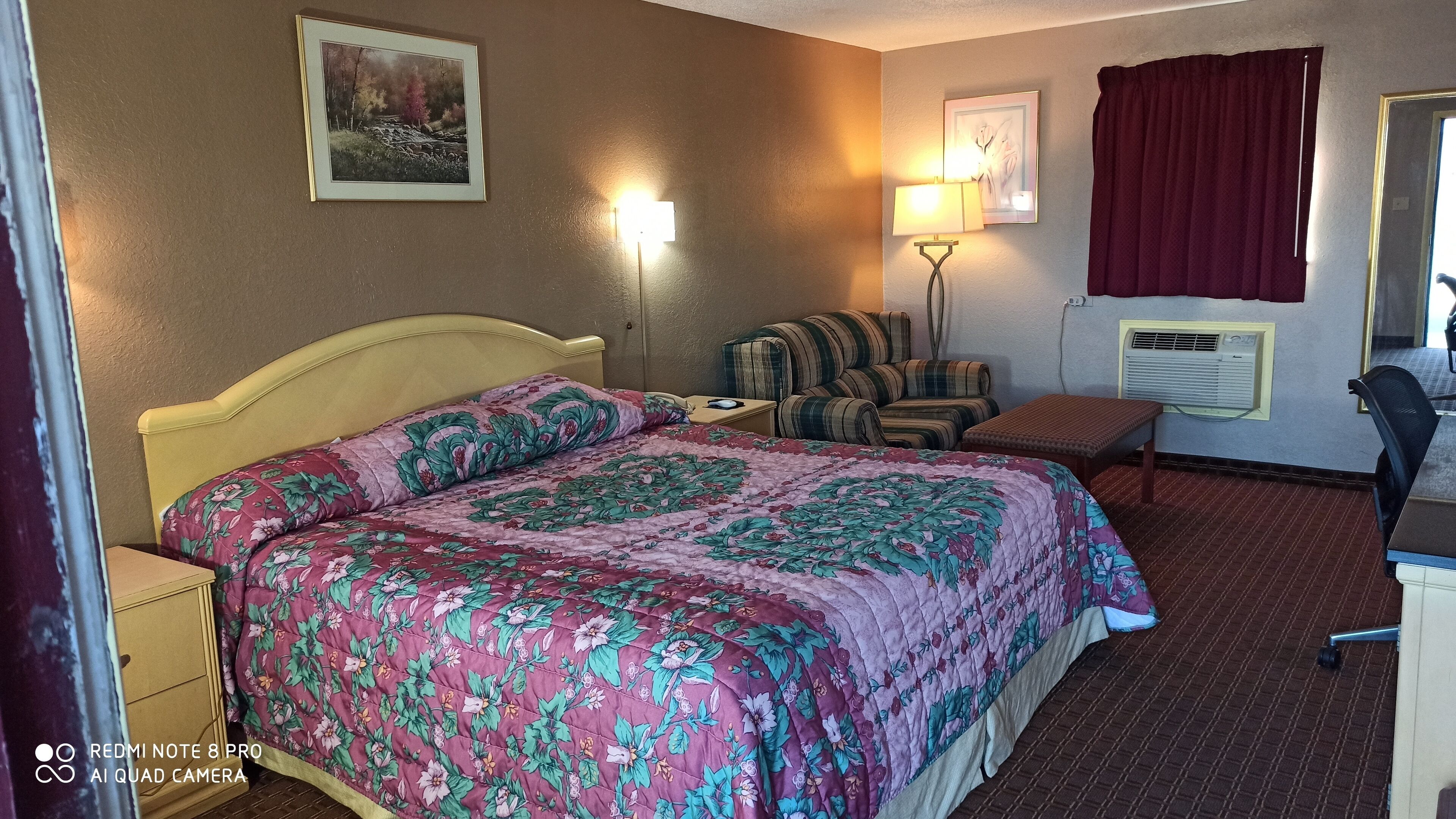 Una habitación de hotel con cama, una silla, un escritorio y una lámpara.