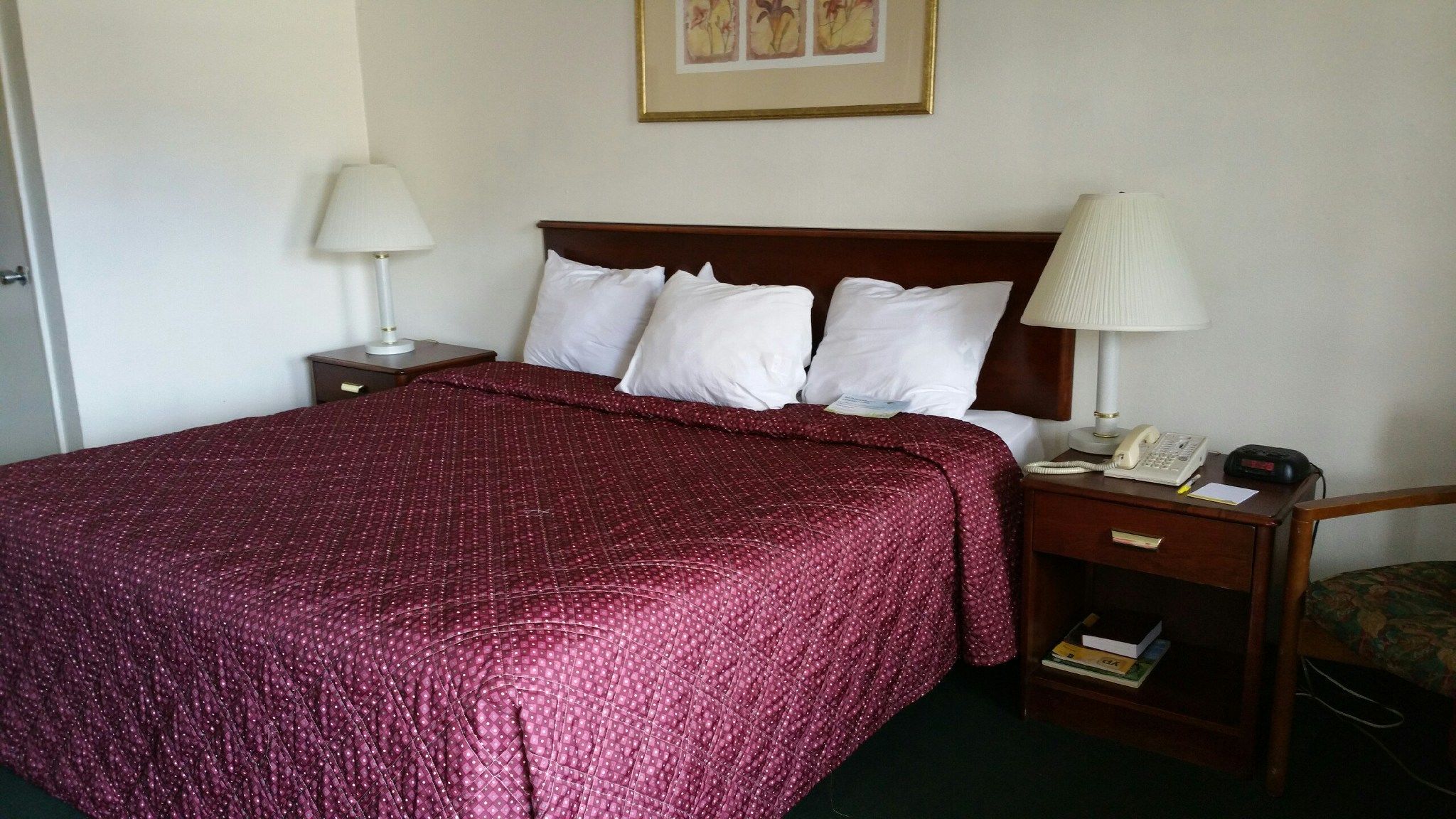 Quarto de hotel com cama bem arrumada, mesa de cabeceira com abajur, telefone e cadeira.