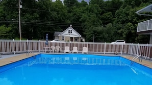 A swimming pool with metal ladders, surrounded by a white fence, with trees and a house in the background. - Best Budget Inn (Tell City)