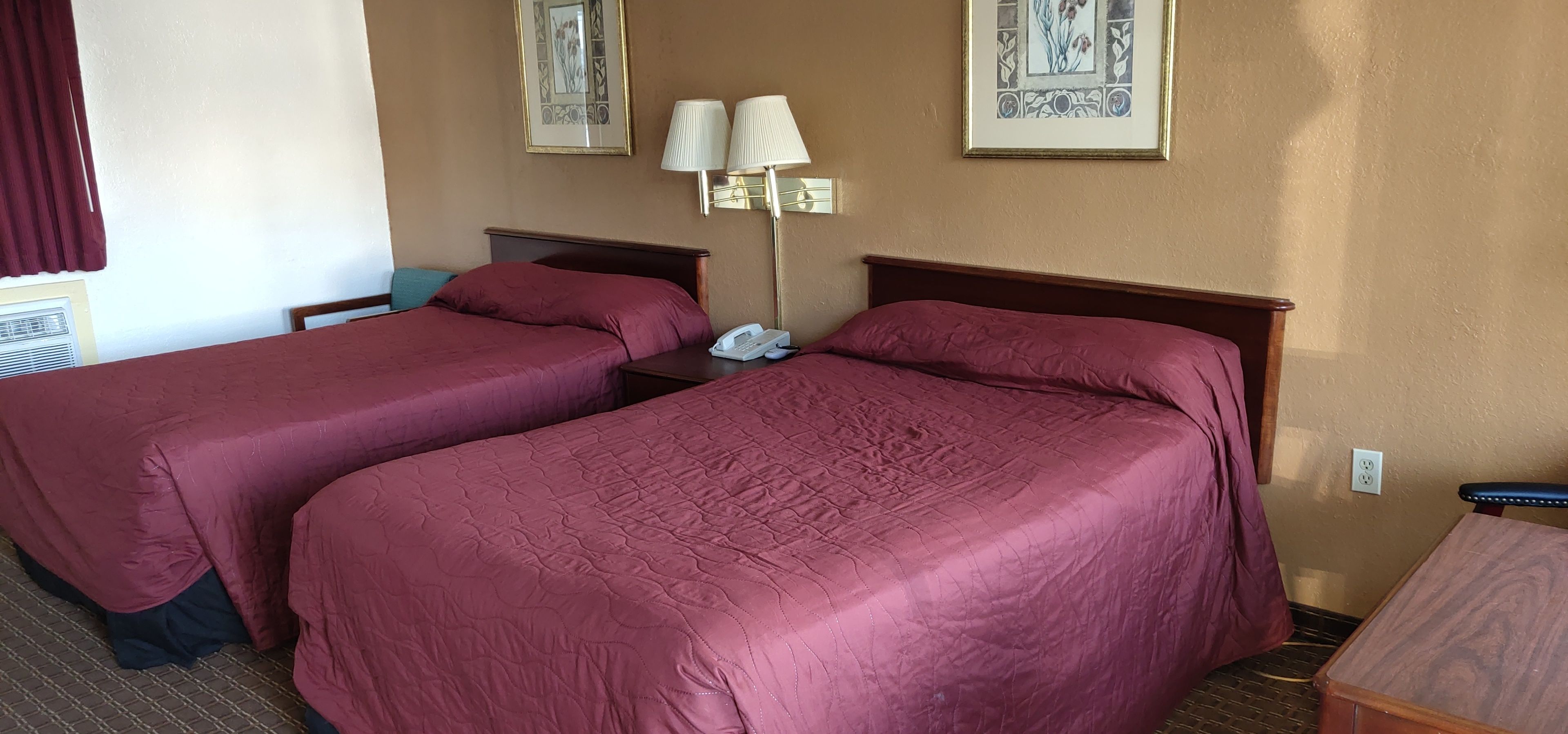 A hotel room with two beds, a bedside table with a lamp, and a telephone.
