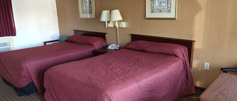 A hotel room with two beds, a bedside table with a lamp, and a telephone.