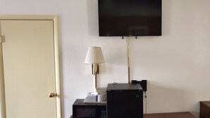 A room with a closed door, a flat-screen TV mounted on the wall, a lamp on a small table, and a microwave. - Best Budget Inn (Tell City)