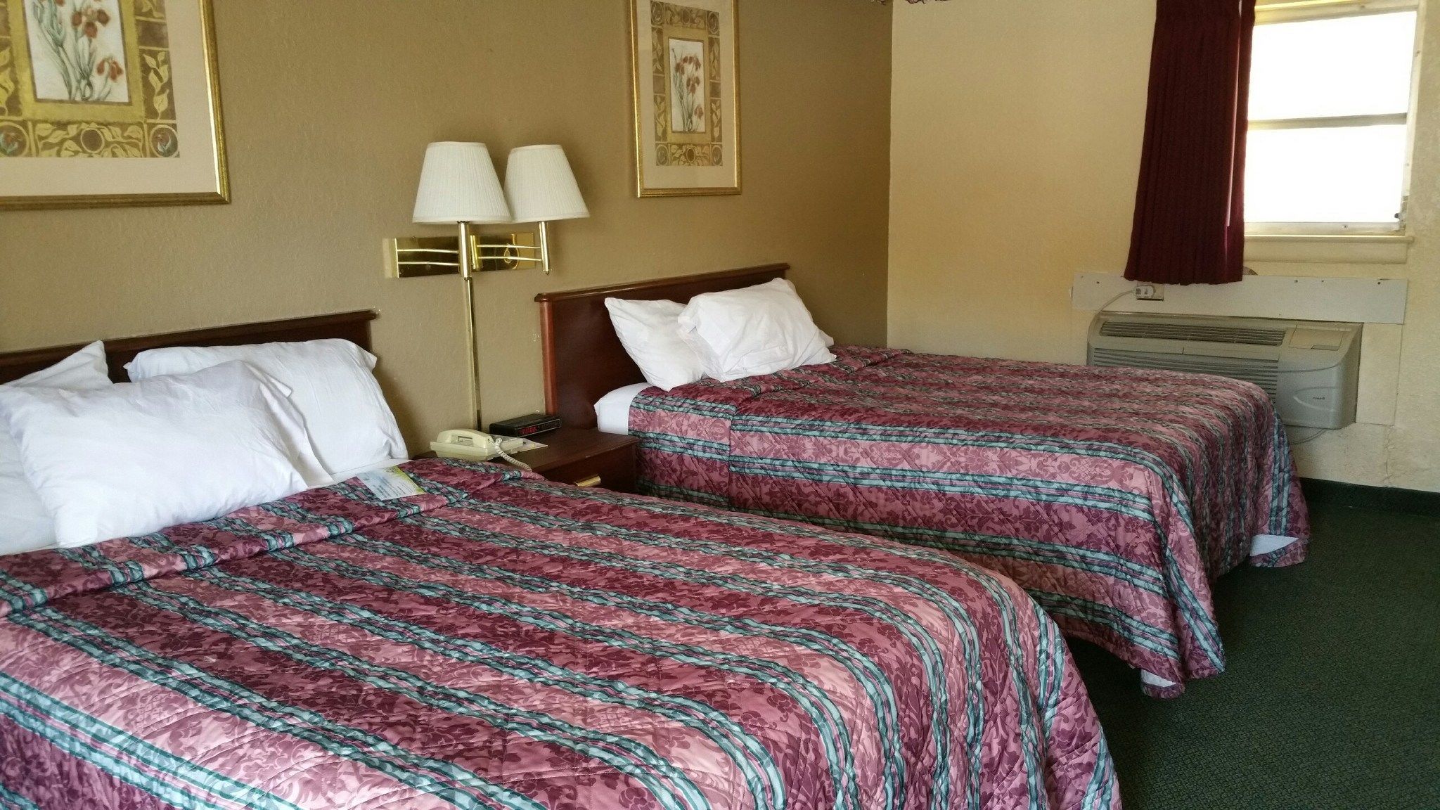 A hotel room with two beds, each with a patterned bedspread, a bedside table with a lamp, and a telephone.
