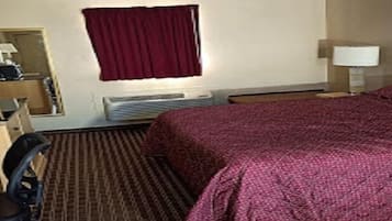 Une chambre d’hôtel avec un lit, un bureau et une chaise, une fenêtre avec un rideau rouge, une lampe et un radiateur.
