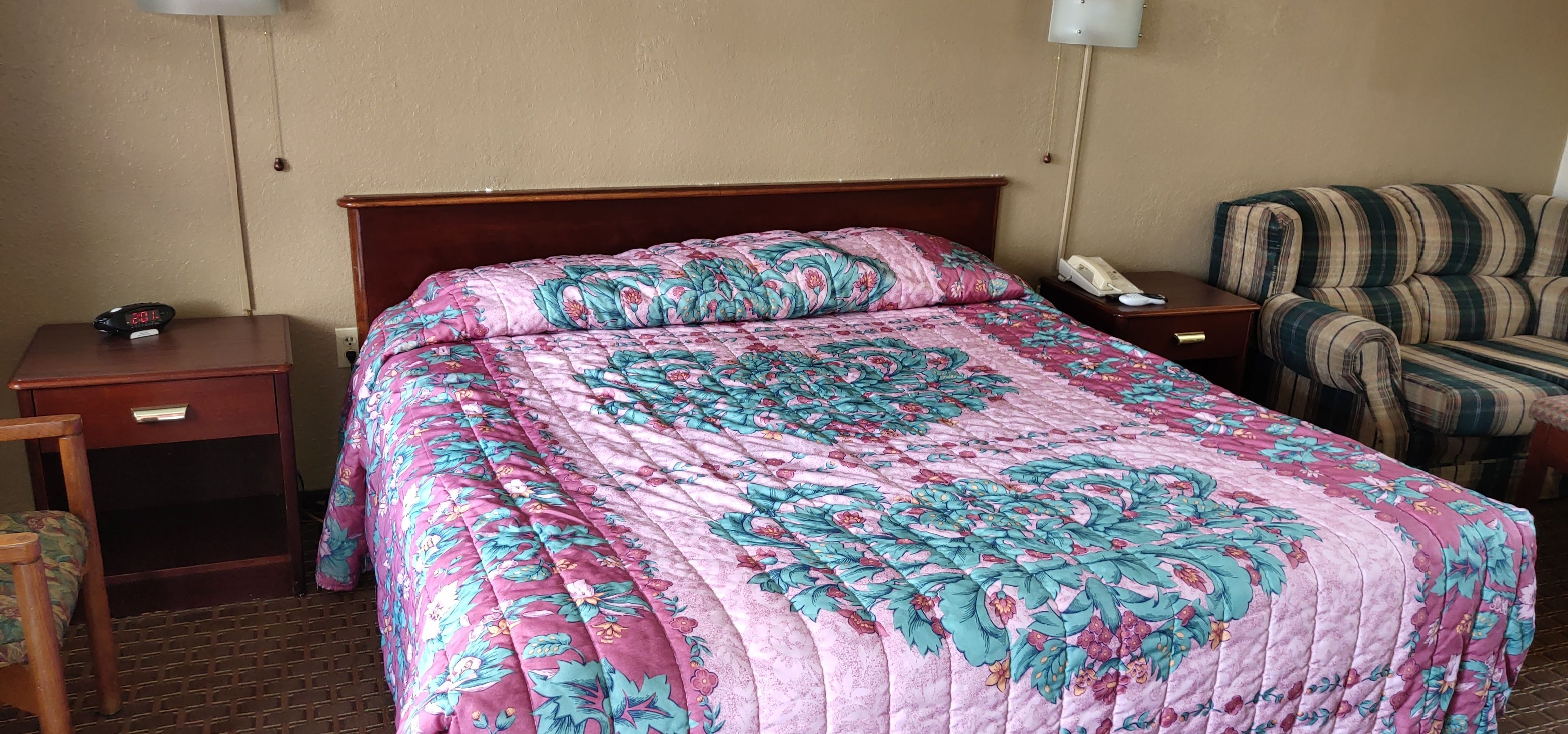 A hotel room with a large bed, a wooden nightstand, a chair, and a telephone.