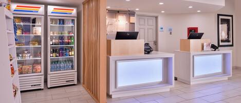 A hotel reception area with a check-in counter, a refrigerator stocked with beverages, and a wooden partition.