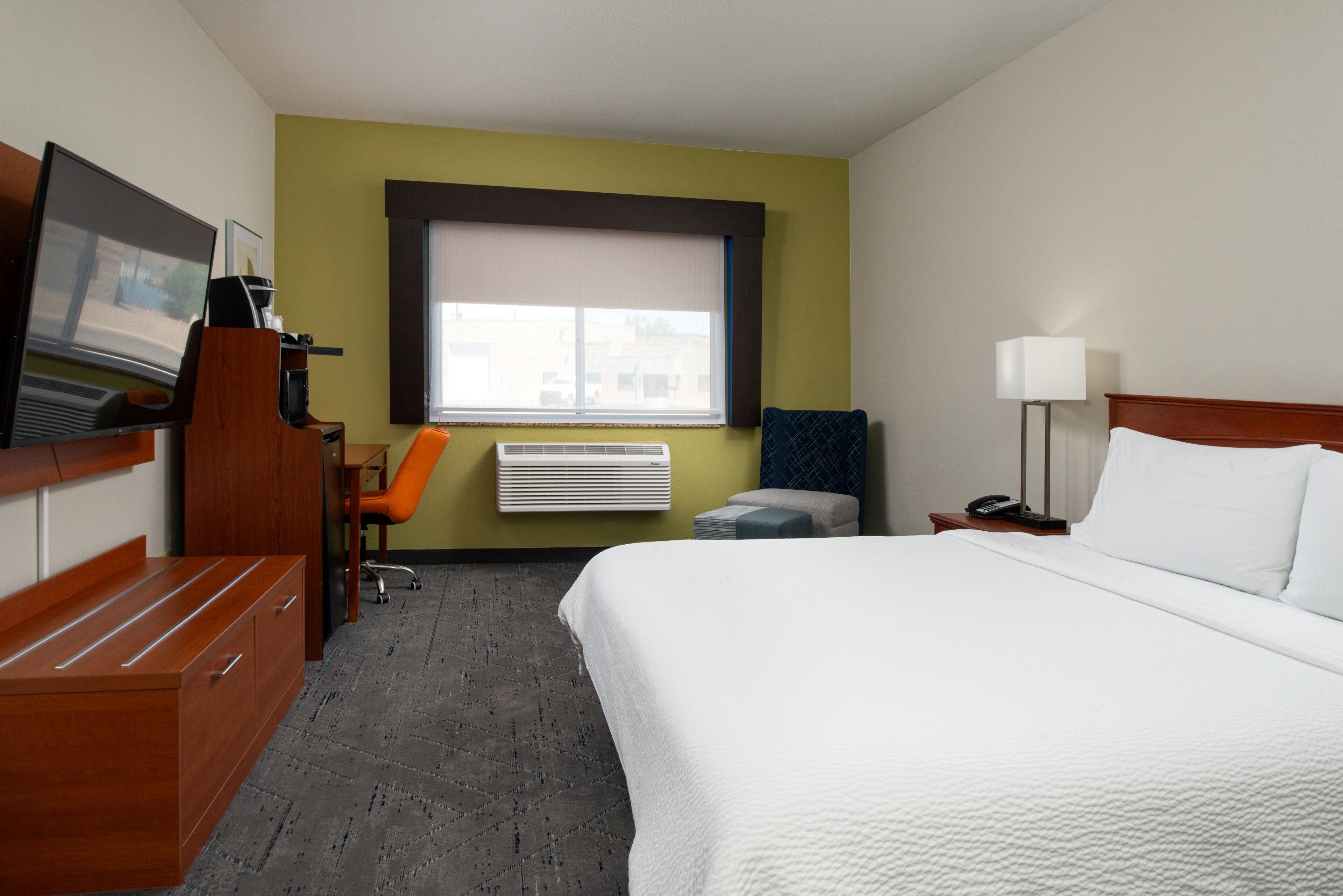 Une chambre d’hôtel comprenant un lit, un bureau avec une télévision, une chaise, une fenêtre et une table de chevet avec une lampe.