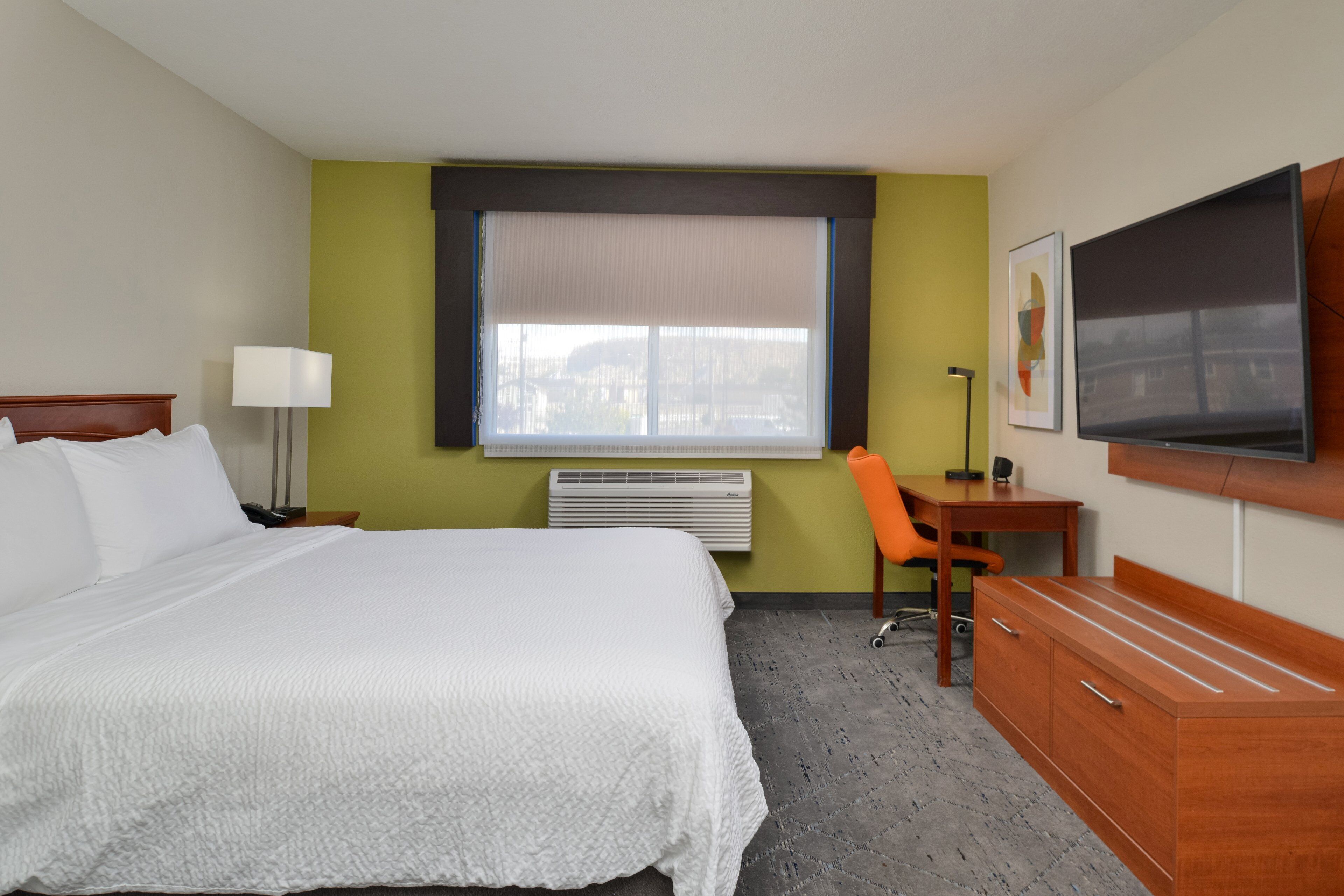 A hotel room with a bed, desk, chair, TV, and a window with a view.