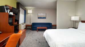 Ein Hotelzimmer mit Bett, Schreibtisch mit Computer, Fernseher, Sofa und einer Kaffeemaschine.