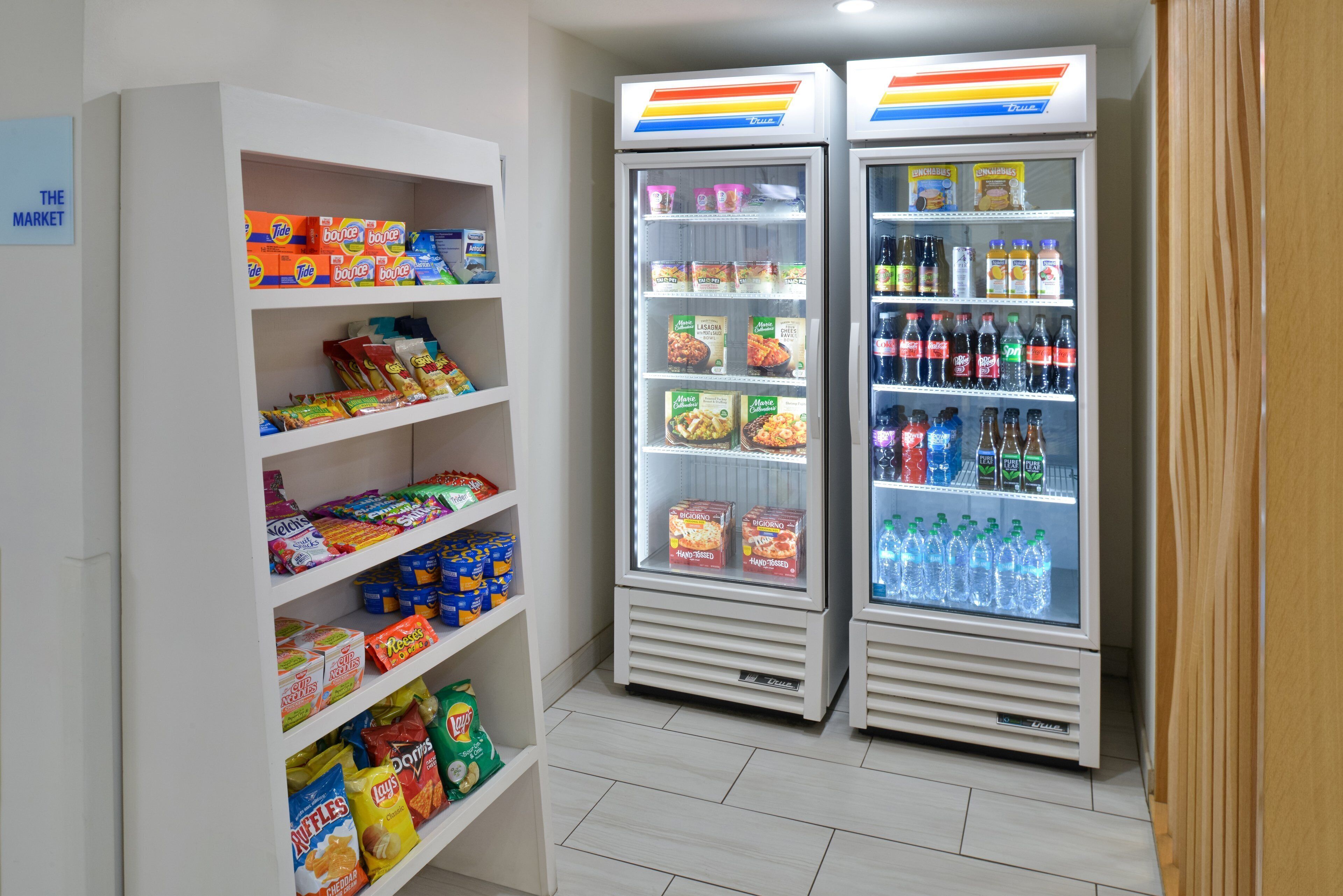 Zona de máquinas expendedoras con opciones de bocadillos y bebidas, incluyendo Tide y Doritos, y una sección refrigerada para bebidas y aperitivos.