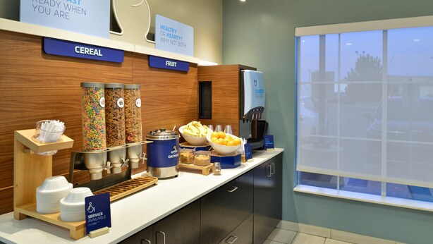 A breakfast bar with cereal, fruit, and a coffee machine.