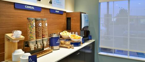 Una barra de desayuno con cereales, fruta y una máquina de café.