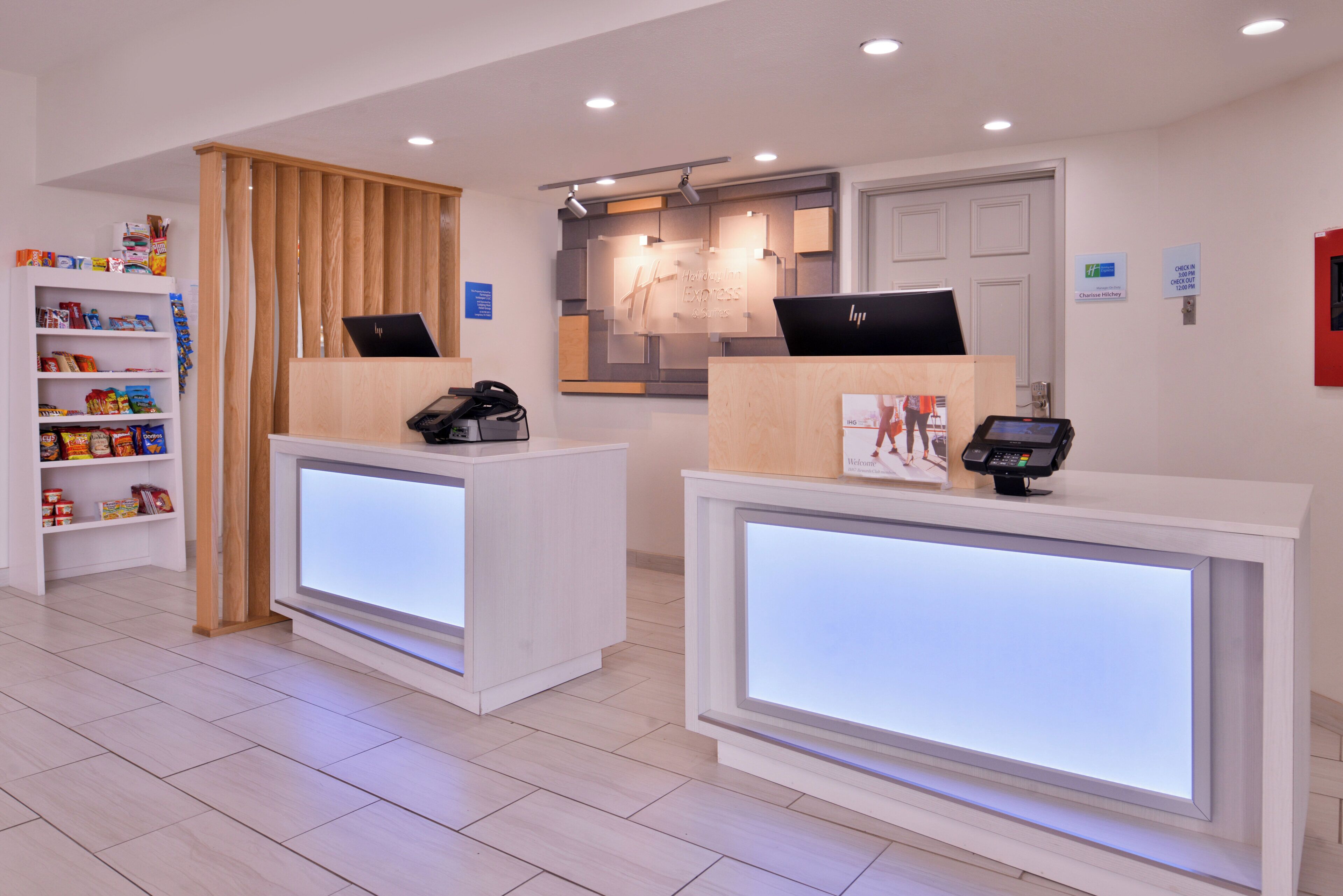 A reception area with two reception desks, a wooden partition, a shelf with snacks, and a sign indicating check-in times.