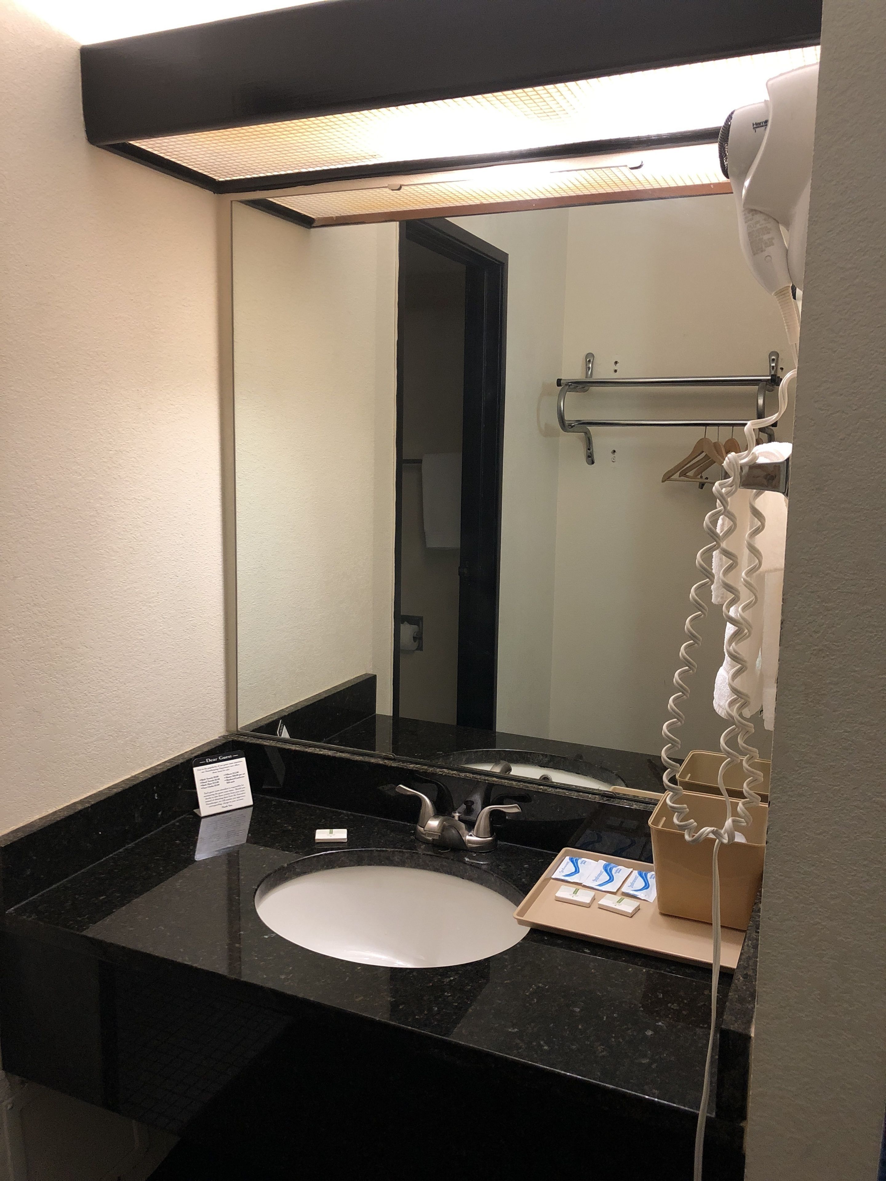 A bathroom with a black countertop, a sink, a mirror, a hairdryer, and a towel rack.