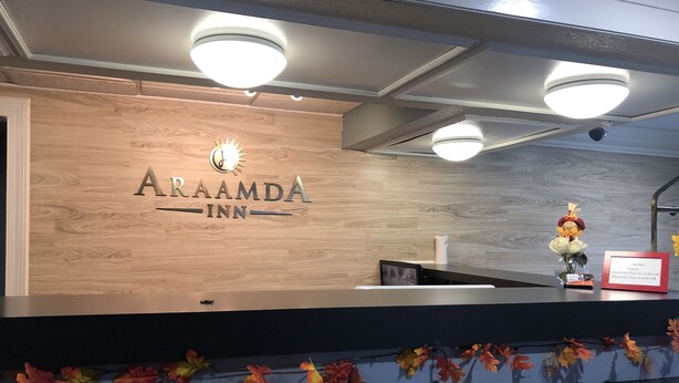 A reception desk at Araamda Inn with a wooden panel design, a sign indicating check-in times, and autumn-themed decorations. - Araamda Inn Norcross (Norcross)