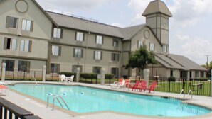 A hotel with a swimming pool, red lounge chairs, and a clock tower. - Araamda Inn Norcross (Norcross)