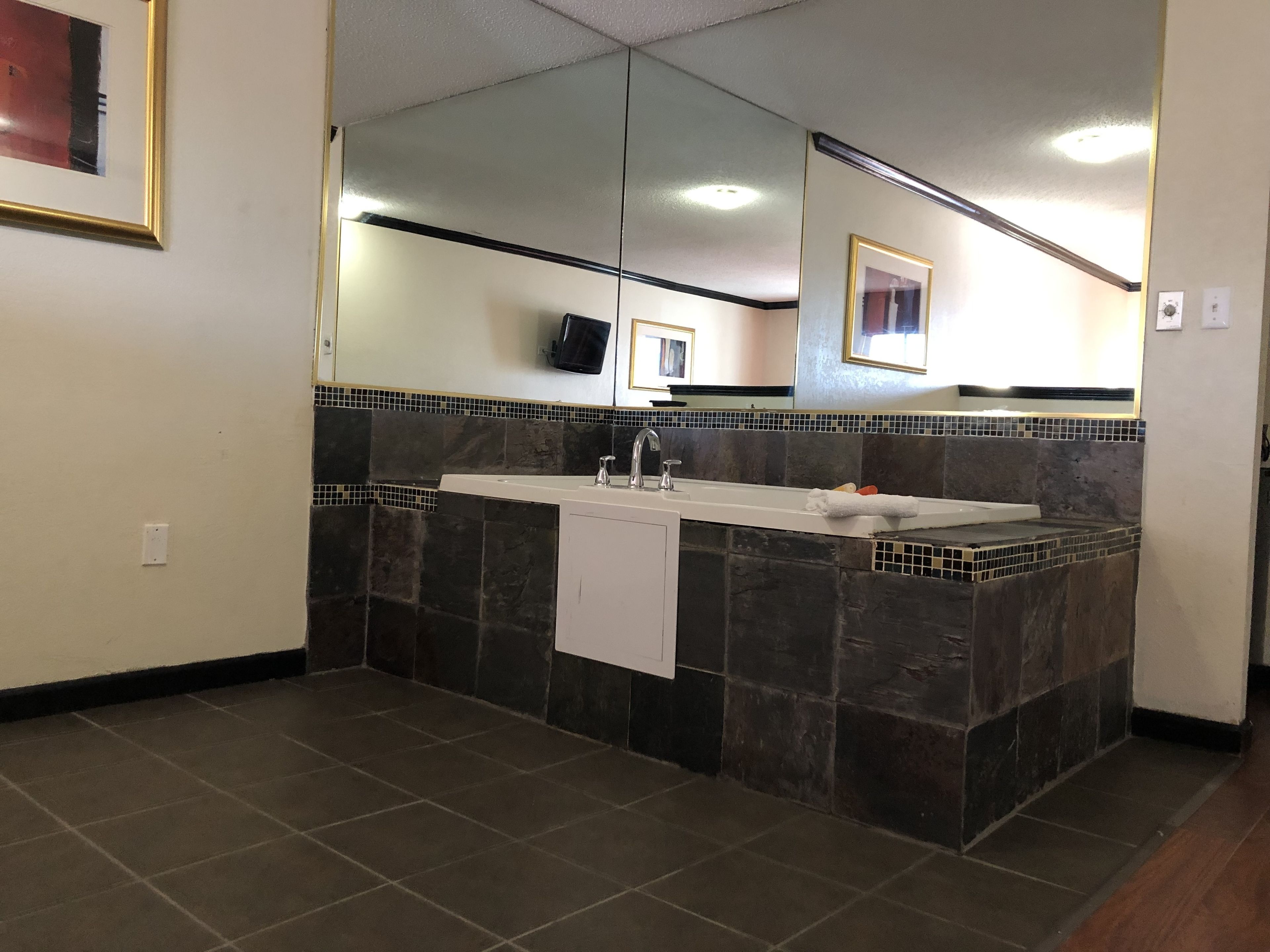 A bathroom with a large mirror, a sink, and dark tiled walls.