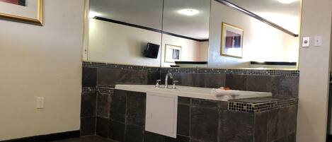 A bathroom with a large mirror, a sink, and dark tiled walls.