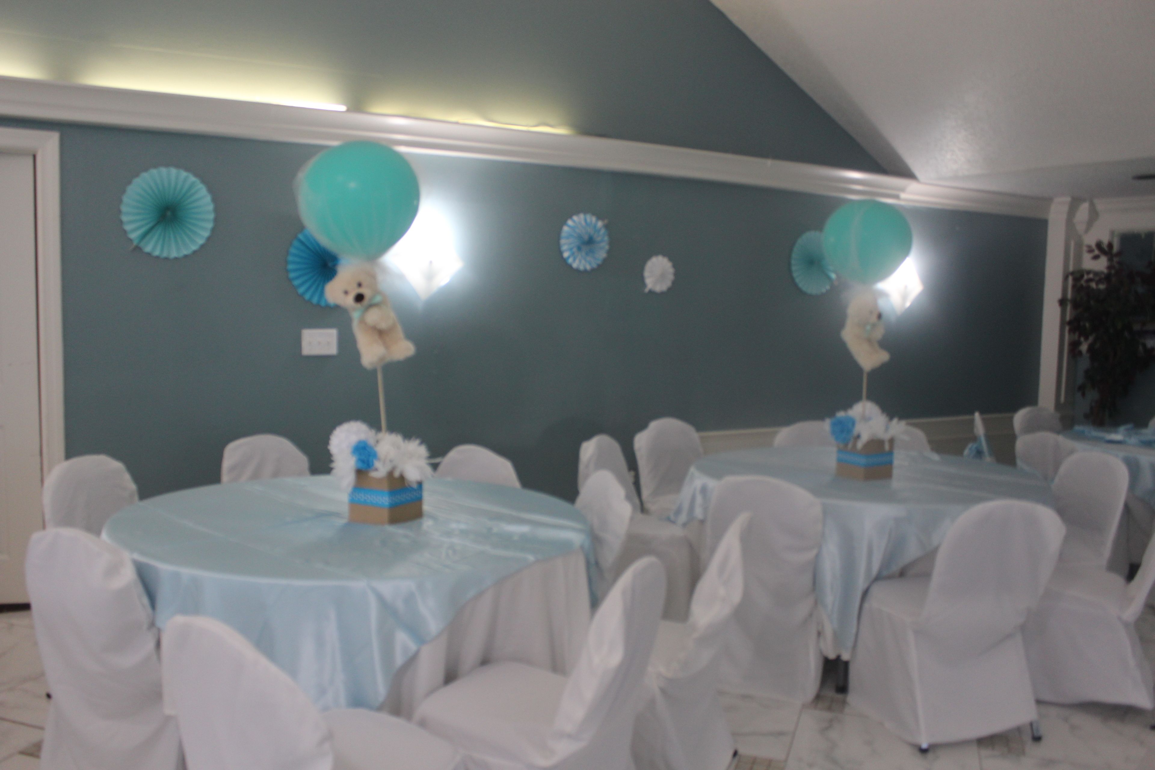 A room with multiple round tables covered with light blue tablecloths, surrounded by white chairs.