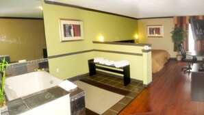 A hotel room with a large bathtub, a bench with towels, a desk, a chair, and two framed pictures on the walls. - Araamda Inn Norcross (Norcross)