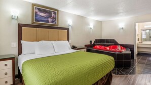 A hotel room with a bed, a red bathtub, a nightstand, and a wall-mounted light fixture. - Econo Lodge Richmond-North Chesterfield (Richmond)