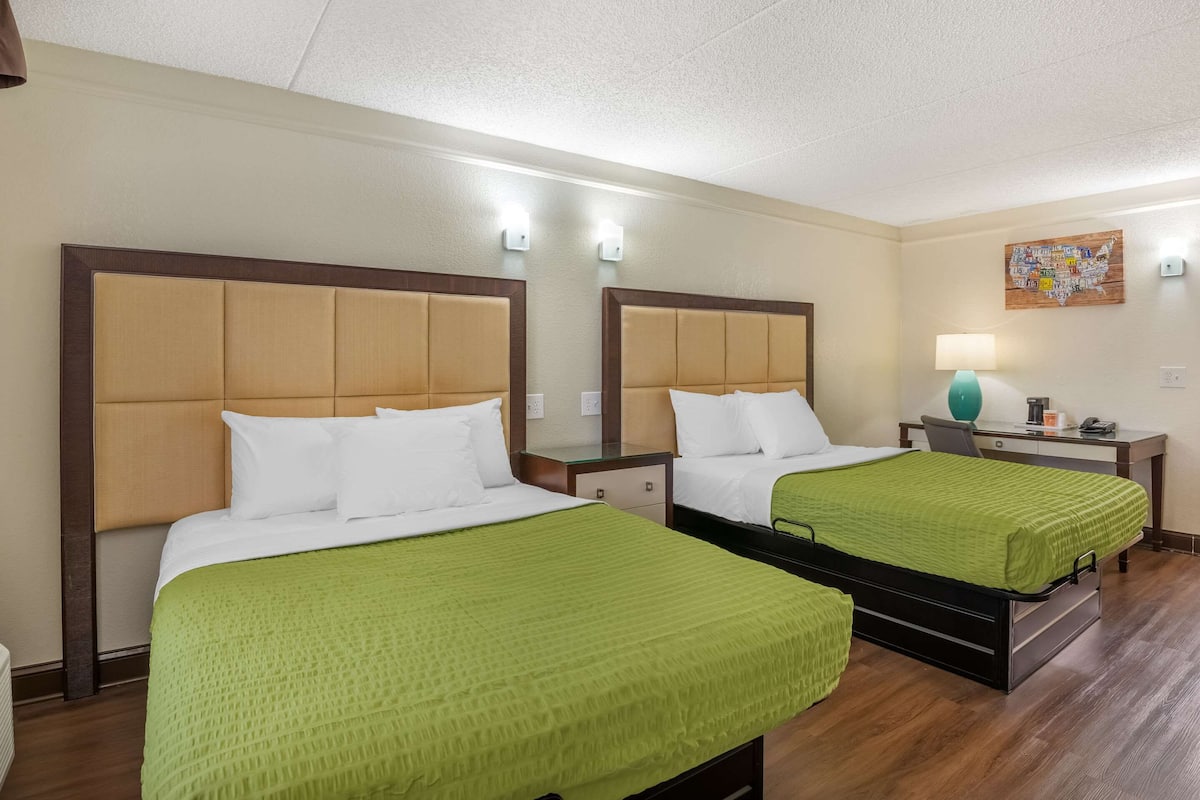 Habitación de hotel con dos camas, cada una con cubrecama verde, cabeceros de madera y mesitas de noche con lámparas.
