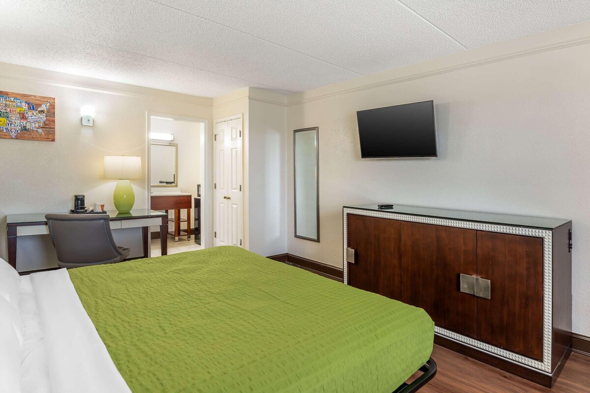 Ein Hotelzimmer mit Bett, Schreibtisch, Stuhl, Fernseher und Kleiderschrank.