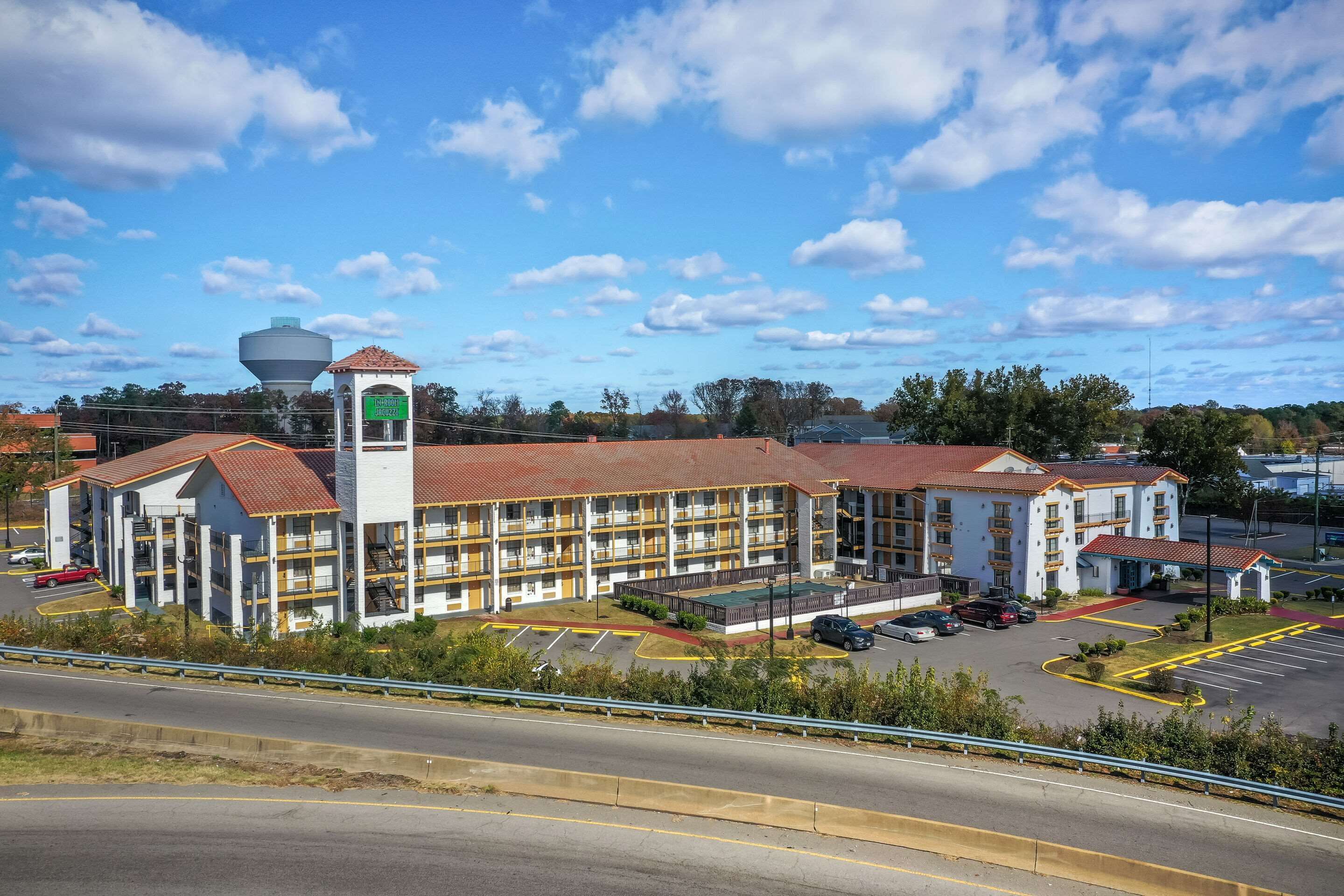 A multi-story hotel with a central tower, a parking lot, and a road in the foreground.