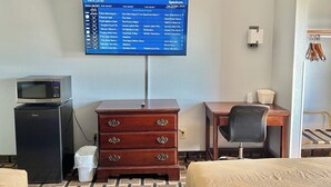 Hotelkamer met een televisie waarop een lokale programmablad staat, een magnetron, een koelkast, een houten dressoir, een bureau en een stoel.