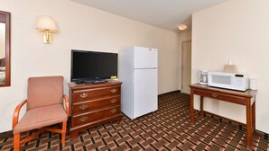 Een hotelkamer met een televisie, koelkast, magnetron, houten dressoir en een kamerbreed tapijt met dessin.