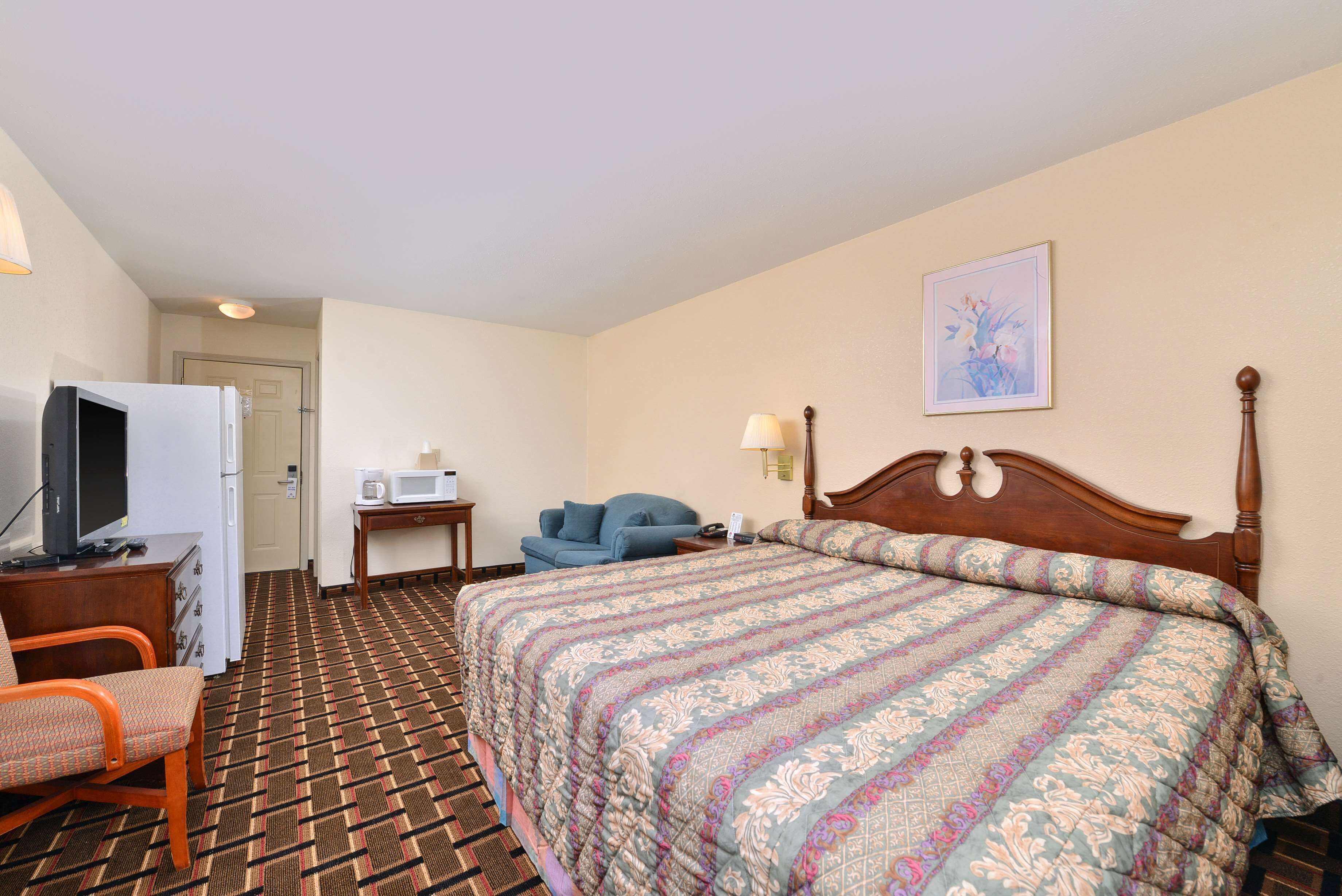 A hotel room with a large bed, a desk with a computer, a chair, a microwave, and a door leading to another room.